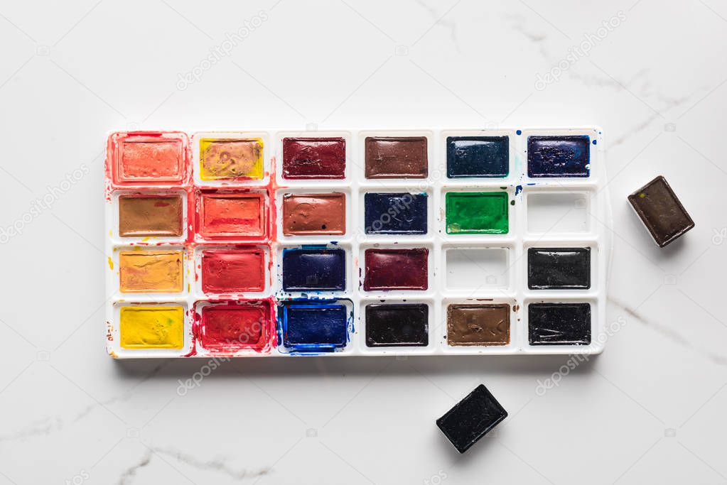 watercolor bright paint palette with missing pieces on marble white surface