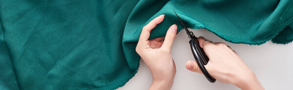 panoramic shot of seamstress cutting colorful fabric with scissors on white background 
