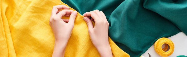 panoramic shot of seamstress sewing colorful fabric with needle on white background 
