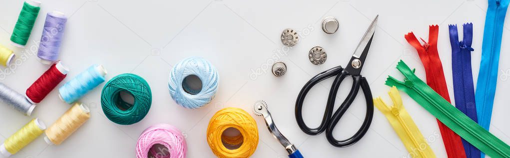 panoramic shot of zippers, scissors, thimbles, threads, knitting yarn balls, bobbins, tracing wheel on white background 