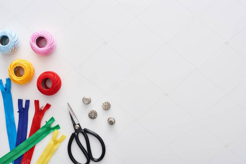 top view of zippers, scissors, thimbles, knitting yarn balls, bobbins on white background 
