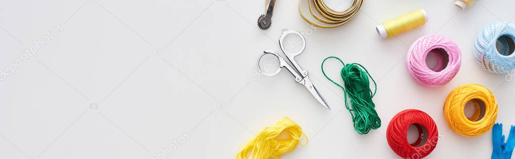 panoramic shot of zipper, scissors, threads, knitting yarn balls, tracing wheel, measuring tape on white background 