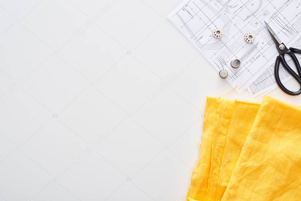 top view of scissors, thimbles, bobbins, fabric and sewing patterns on white background 