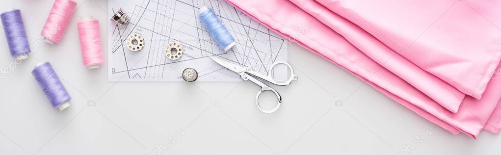 panoramic shot of fabric, sewing pattern, scissors, thimbles, bobbins and threads on white background 