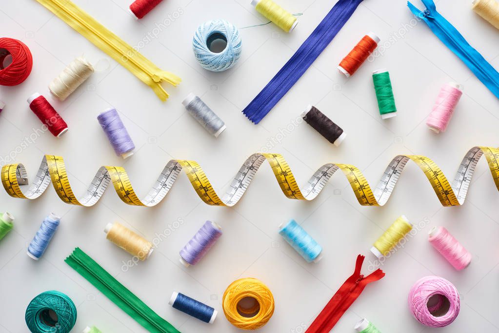 top view of measuring tape, colorful threads and zippers on white background 