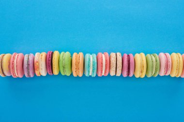 top view of multicolored delicious French macaroons in row on blue bright background clipart