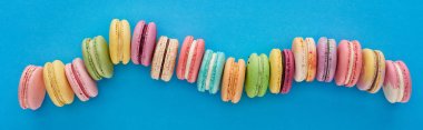 mavi parlak arka plan üzerinde kavisli çizgi de çok renkli lezzetli Fransız macaroons üst görünümü, panoramik çekim
