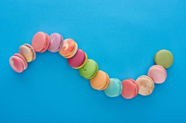kopya alanı ile mavi parlak arka plan üzerinde kavisli çizgi de çok renkli lezzetli Fransız macaroons üst görünümü