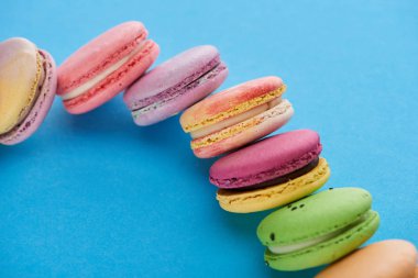 düz mavi parlak arka plan üzerinde çok renkli lezzetli Fransız macaroons ile yatıyordu