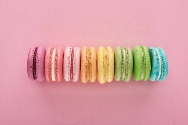 top view of colorful fresh delicious French macaroons in line on pink background clipart