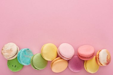 top view of multicolored delicious French macaroons on pink background with copy space clipart