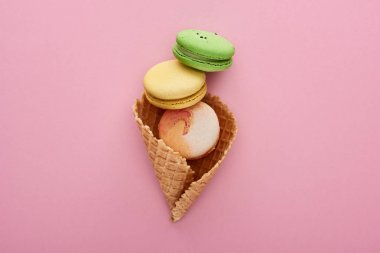 pembe arka plan üzerinde gevrek waffle koni içinde çok renkli lezzetli Fransız macaroons üst görünümü