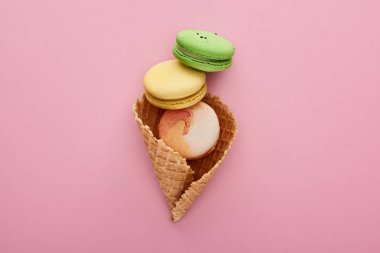 top view of multicolored delicious French macaroons in crispy waffle cone on pink background clipart