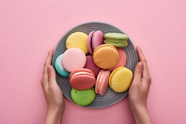 pembe arka plan üzerinde çok renkli lezzetli Fransız macaroons plaka tutan kadın kırpılmış görünümü