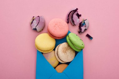 pembe arka plan üzerinde mavi posta zarfı içinde çok renkli lezzetli Fransız macaroons üst görünümü