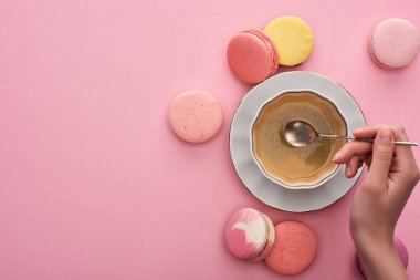 pembe arka plan üzerinde lezzetli Fransız macaroons yakın kahve fincanı üzerinde gümüş kaşık tutan kadın kırpılmış görünümü