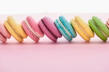 row of delicious colorful French macaroons of different flavors on pink background with copy space clipart