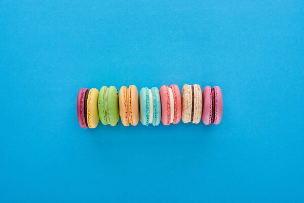 top view of multicolored delicious French macaroons in line on blue bright background