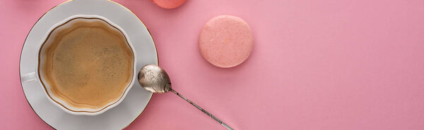 top view of delicious French macaroons near coffee with silver spoon on pink background with copy space, panoramic shot