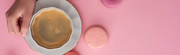 cropped view of woman drinking coffee with delicious French macaroons on pink background, panoramic shot