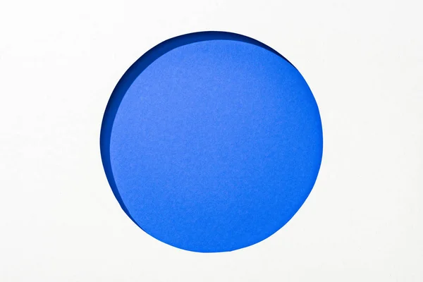 在电蓝色彩色背景上在白纸上切出圆孔 — 图库照片