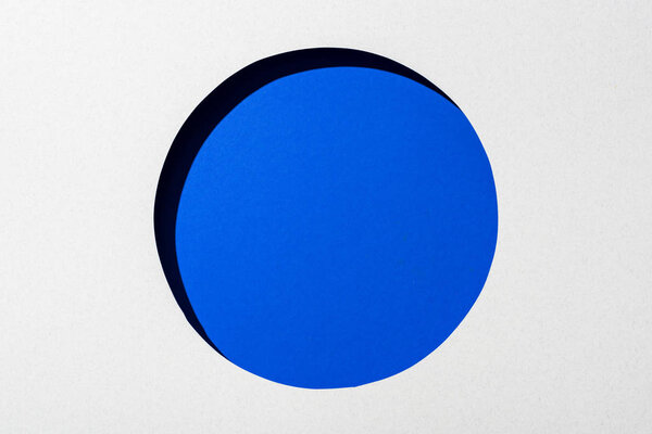 вырезать круглое отверстие в белой бумаге на электрическом синем фоне
