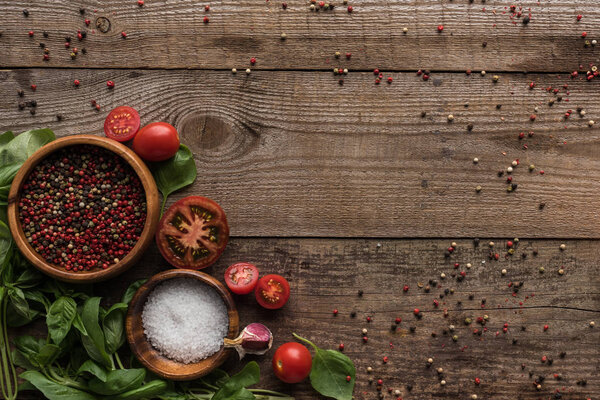 top view of scattered pepper near sliced cherry tomatoes, spinach and bowls on wooden table 