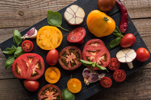 top view of sliced yellow and cherry tomatoes with spinach, garlic and chilli pepper on black wooden tray 