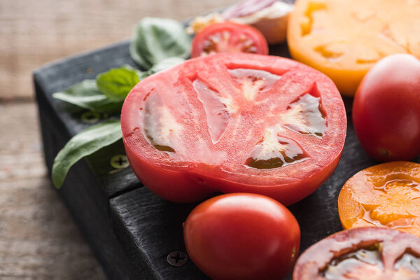close up view of sliced red and yellow tomatoes with spinach on black tray on wooden table 