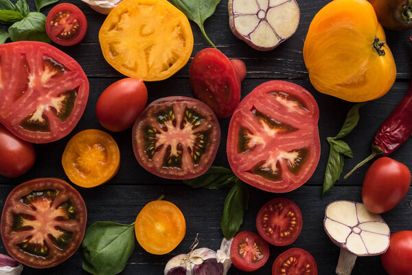 top view of scattered chilli pepper, spinach, sliced tomatoes and garlic on black tray on wooden table 