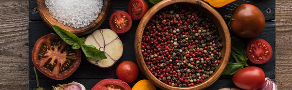 panoramic shot of bowls with pepper and salt near chilli pepper, spinach, sliced tomatoes and garlic on black tray on wooden table 