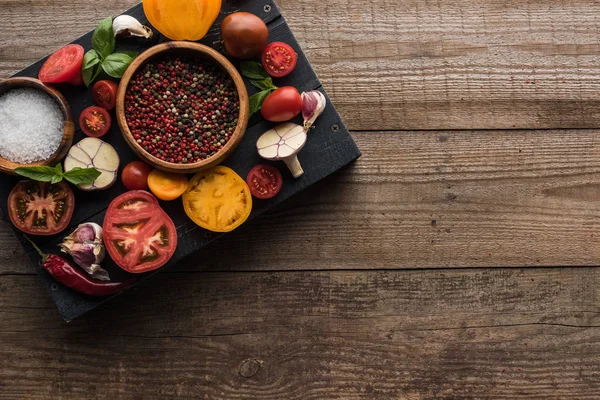 Top view of black tray with bowls with pepper and salt near chilli pepper, spinach, sliced tomatoes and garlic on wooden table — Stock Image Top View Black Tray Bowls Pepper Salt Chilli Pepper Spinach Stock Photo