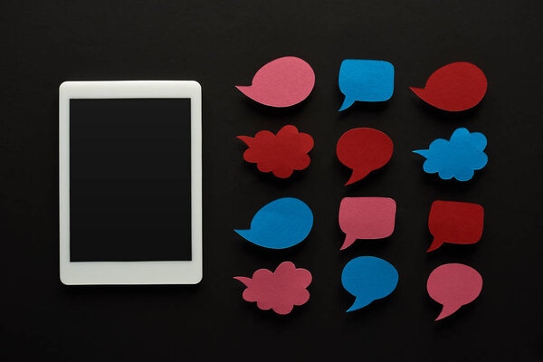 top view of digital tablet with blank screen on black background near empty speech bubbles, cyberbullying concept