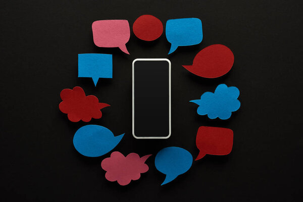 top view of smartphone on black background with empty speech bubbles, cyberbullying concept