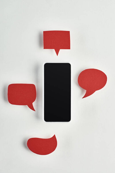 top view of smartphone with blank screen on white background near empty red speech bubbles, cyberbullying concept