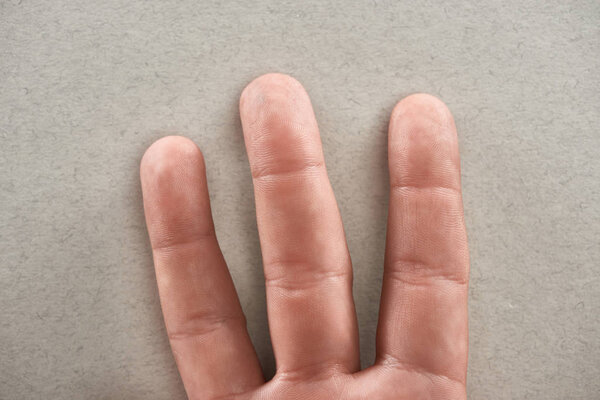 частичный вид человека, показывающий три пальца на сером фоне
