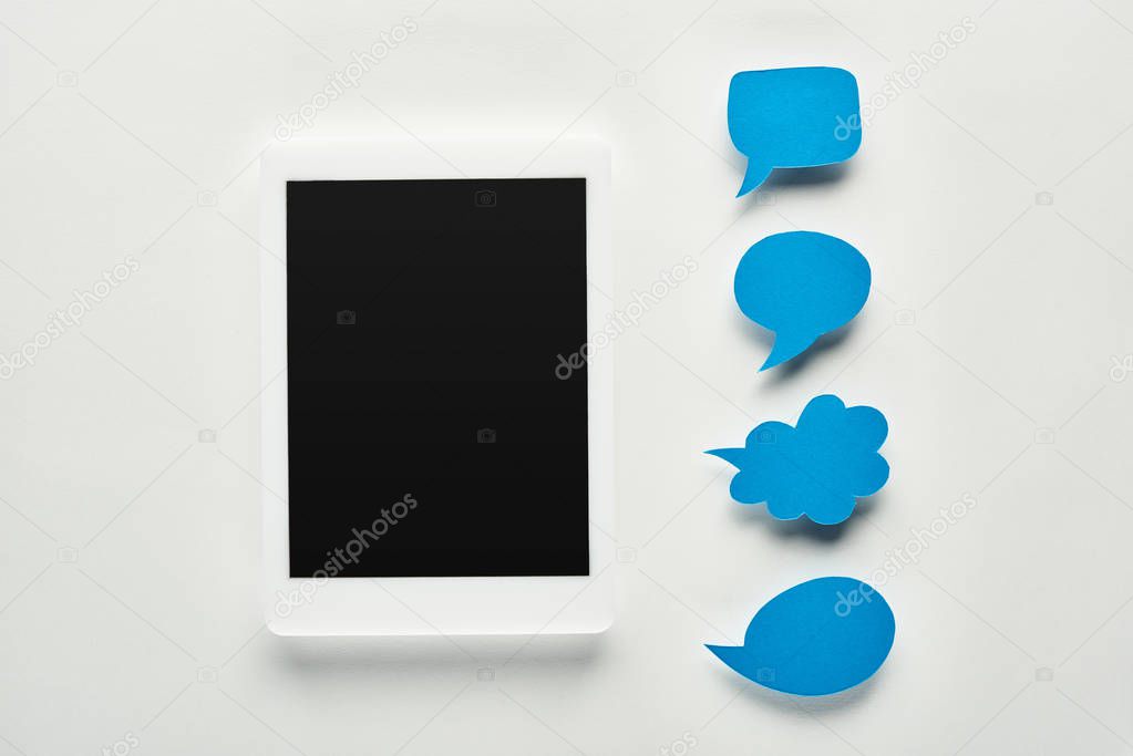 top view of digital tablet with blank screen on white background near empty blue speech bubbles, cyberbullying concept