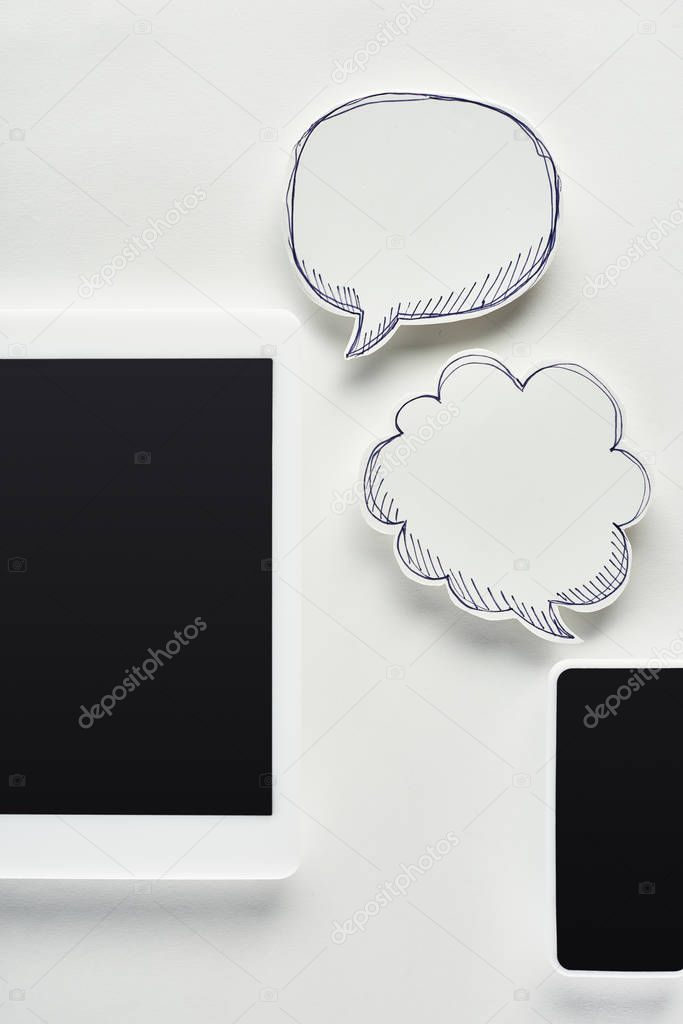 top view of digital tablet and smartphone on white background near empty speech bubbles, cyberbullying concept