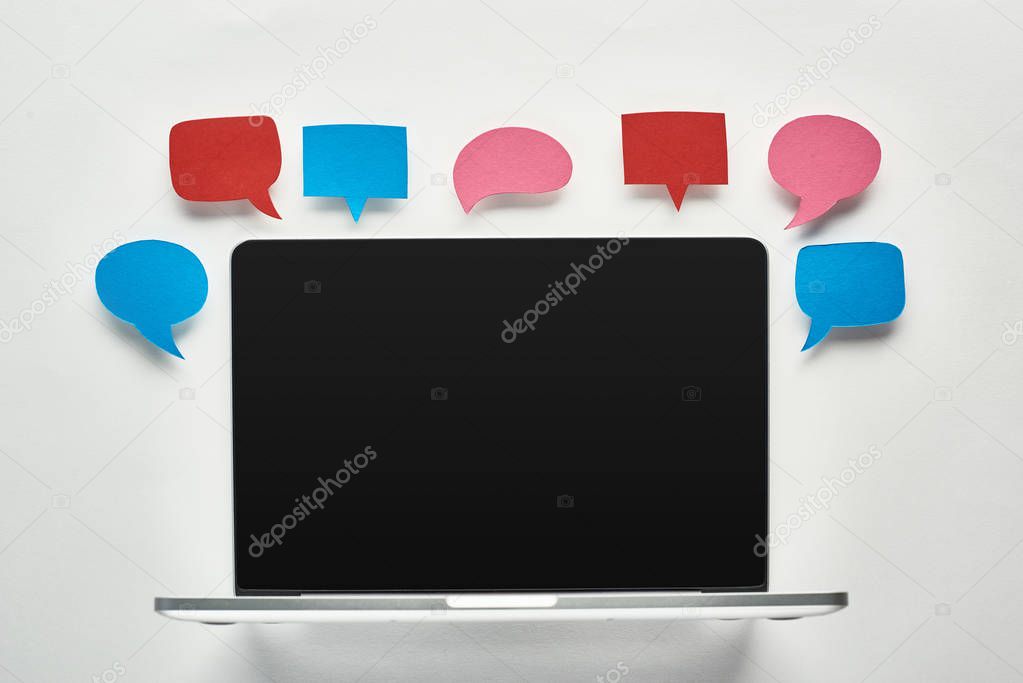 laptop with blank screen on white background near empty colorful speech bubbles, cyberbullying concept