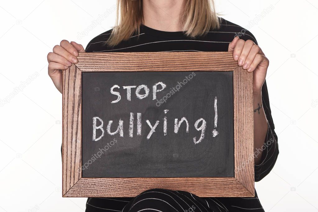 cropped view of girl holding chalkboard in wooden frame with stop bullying lettering isolated on white
