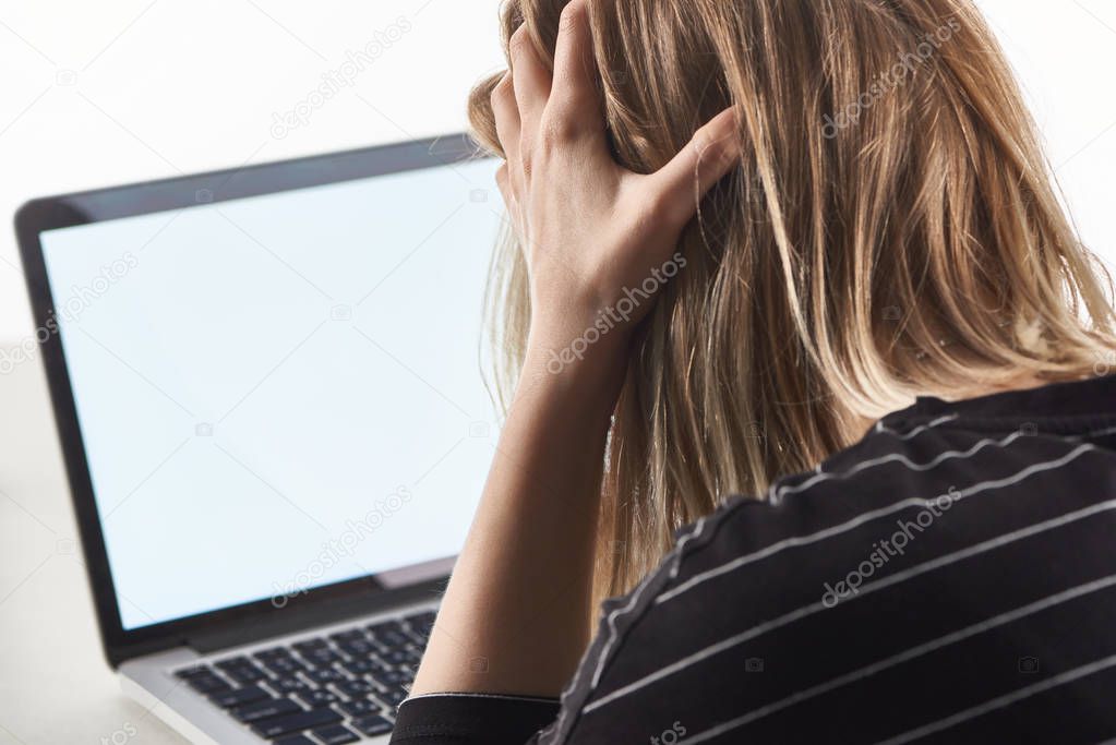 offended blonde girl as victim of cyberbullying sitting near laptop with blank screen