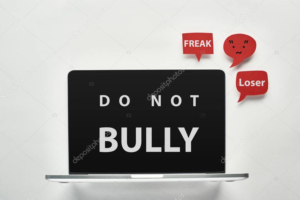 laptop with do not bully lettering on screen on white background near red speech bubbles with offensive words, cyberbullying concept