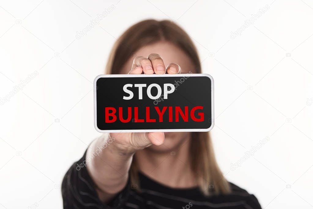 selective focus of victim of cyberbullying showing smartphone with stop bullying lettering on screen isolated on white
