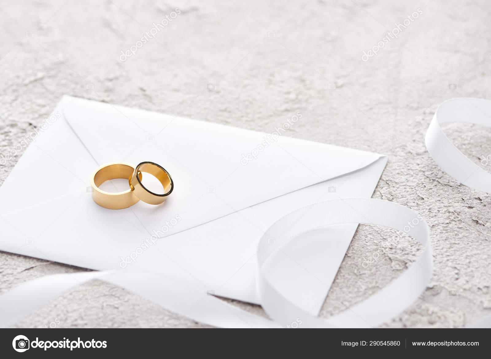 golden-rings-envelope-white-ribbon-grey-textured-surface-stock-photo