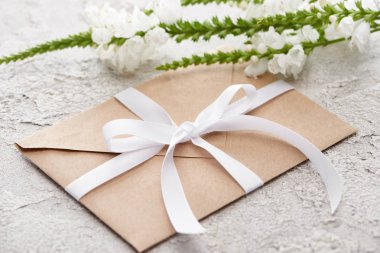 beige envelope with white ribbon near flowers on grey textured surface   clipart