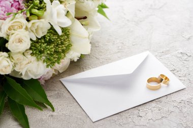 dokulu yüzeyde çiçek buketi yanında beyaz zarf üzerinde alyans 
