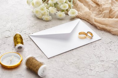 bobinler, krizantem, bej çuval bezi ve dokulu yüzeyüzerinde altın pusula yakınında beyaz zarf üzerinde altın halkalar 