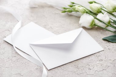 gri dokulu yüzeyde eustoma çiçekleri ve beyaz kurdele yakınında beyaz zarf  