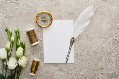 altın pusula, bobinler ve gri dokulu yüzeyüzerinde beyaz eustoma çiçekleri yakın beyaz kart üzerinde quill kalem üst görünümü