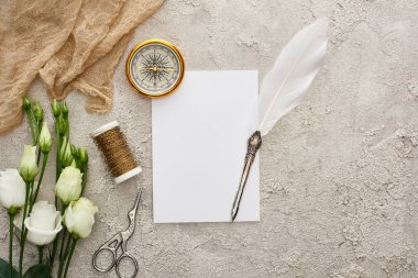 altın pusula, bej çuval bezi, bobin, makas ve gri dokulu yüzeyüzerinde beyaz eustoma çiçekleri yakın boş kart üzerinde quill kalem üst görünümü